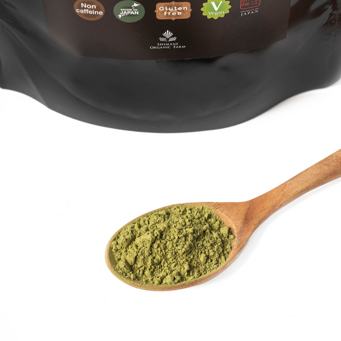 A spoon of mulberry matcha powder in front of a package bag of the product