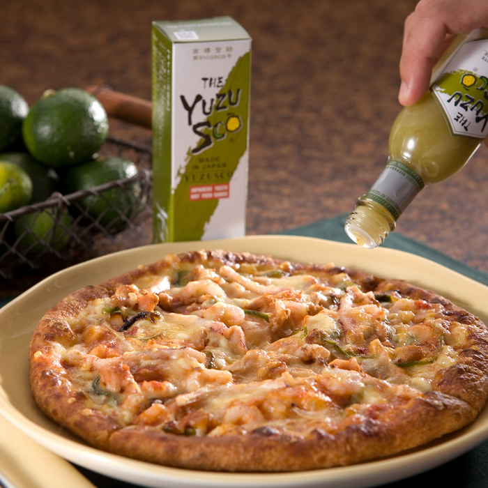 Man pouring yuzu hot sauce onto a whole pizza