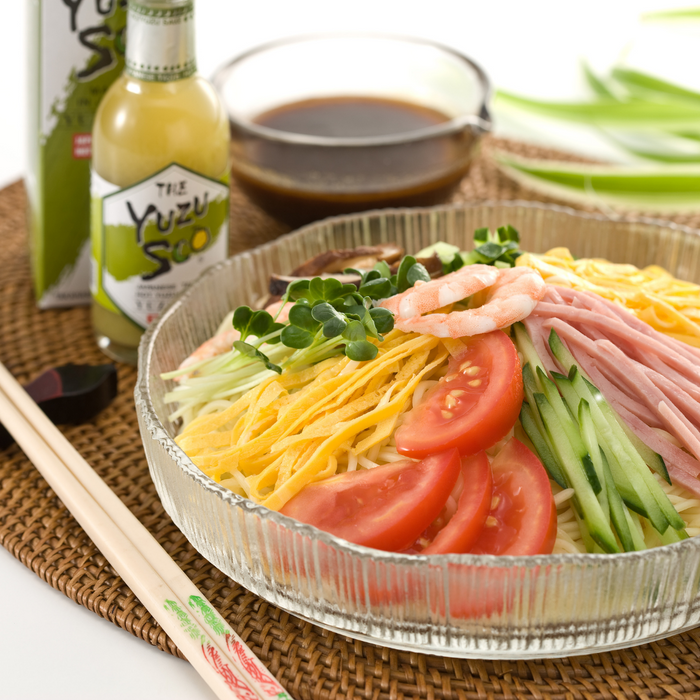 A glass bowl of cold noodle dish next to a bottle of the product