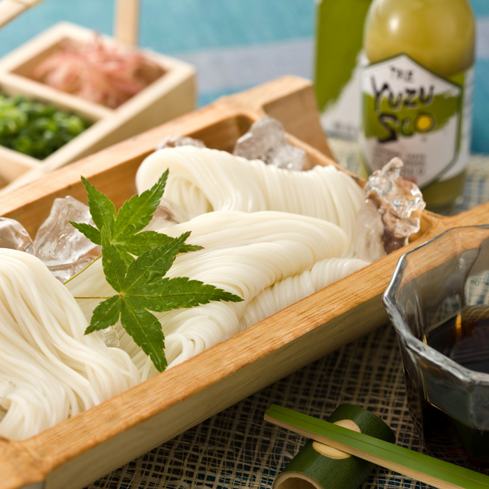 A bamboo bowl of cold noodle dish next to a bottle of the product