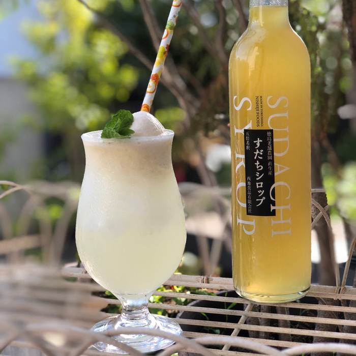 A glass of sudachi soda next to a bottle of the product