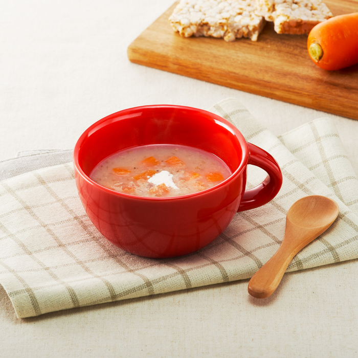 A cup of carrot soup next to carrot and rice crackers