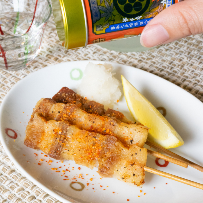 Man sprinkling ichimi pepper onto skewers