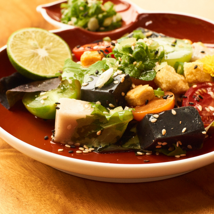 A bowl of salad with sesame tofu and black sesame tofu