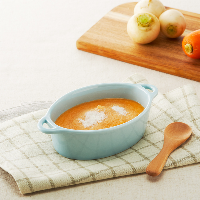 A cup of vegetable soup next to carrots and radishes