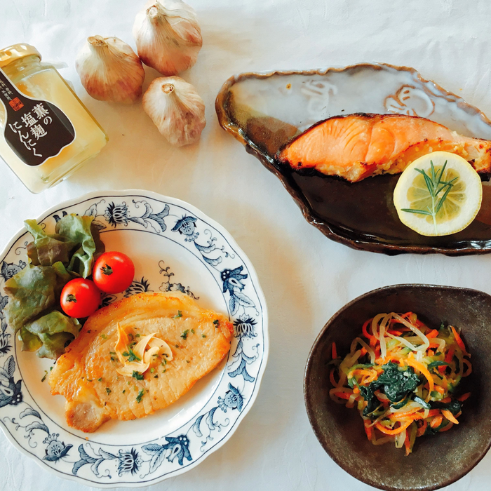 A plate of grilled pork, a plate of grilled salmon and a bowl of mixed vegetables