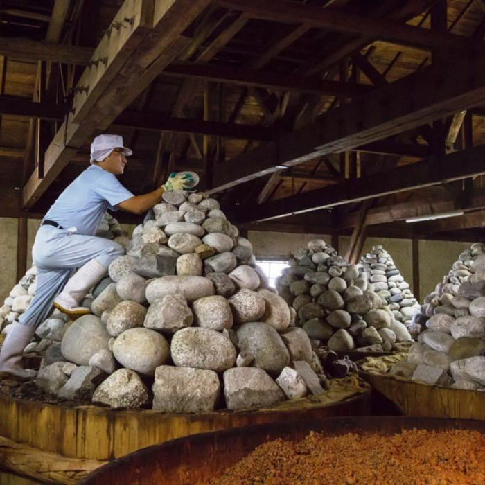 A craftsman piling up big stones on miso barrels