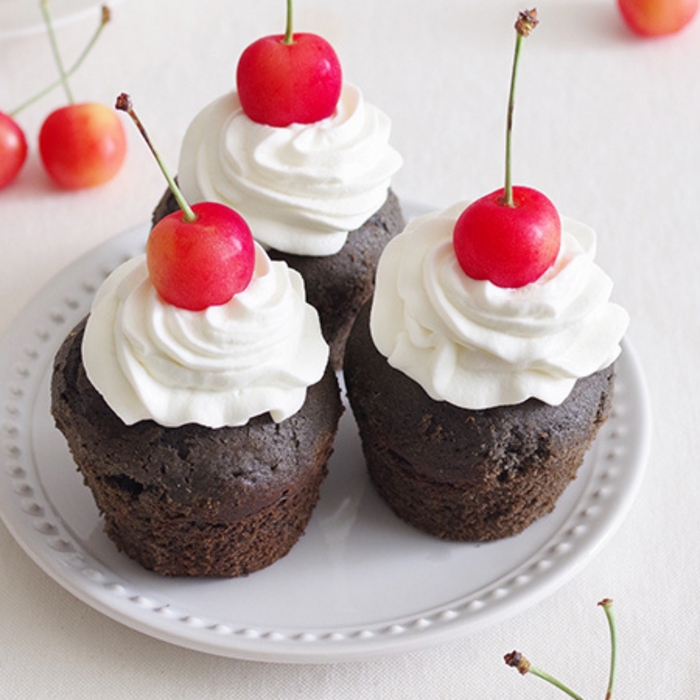 Black sesame cupcakes topped with whipped cream and cherries on a plate