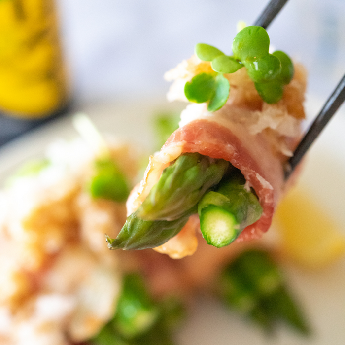 Man taking grilled asparagus rolled with bacon with chopsticks