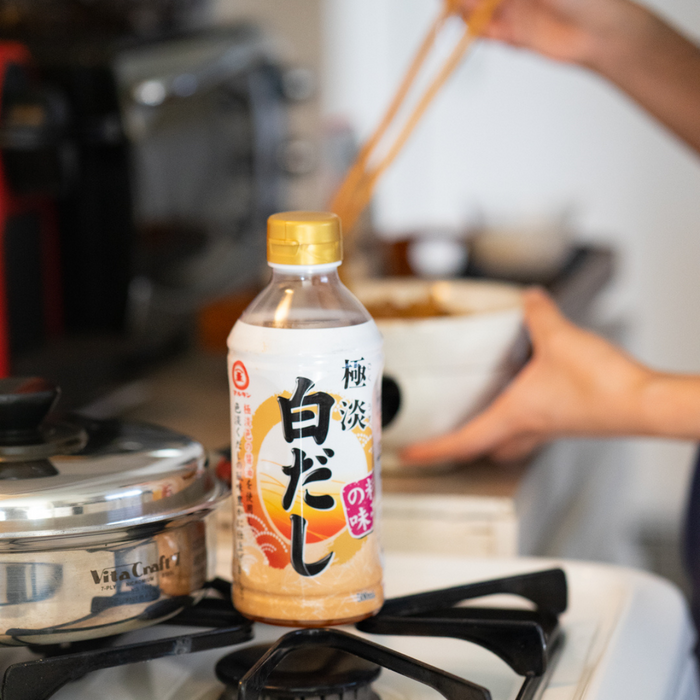 A bottle of shiro dashi next to man cooking in kitchen
