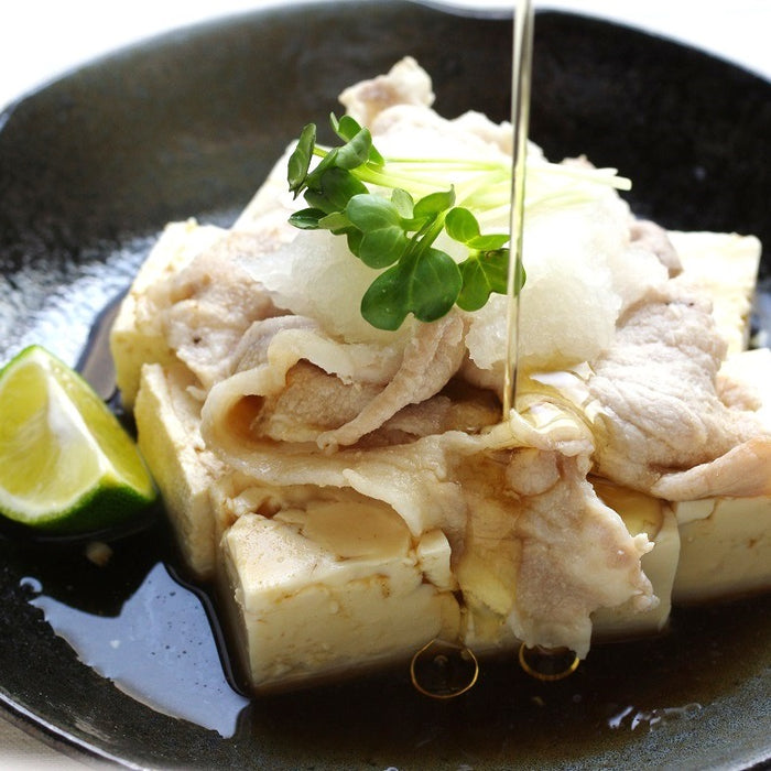 A plate of tofu and boiled pork being drizzled with sesame oil