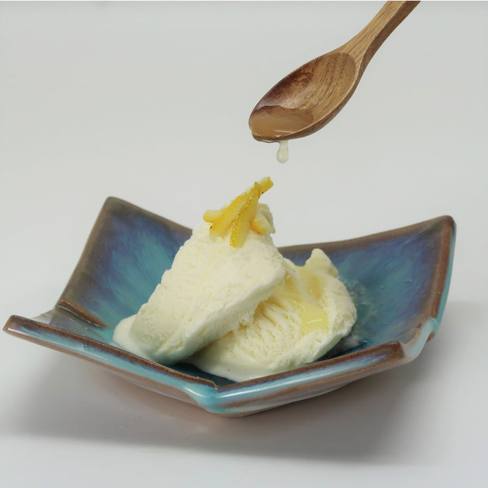 A plate of vanilla ice cream being poured with yuzu syrup from wooden spoon