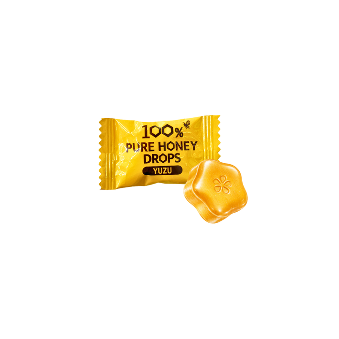 A yellow candy wrapper labeled '100% Pure Honey Drops Yuzu' next to a small yellow flower-shaped honey drop on a plain white background.