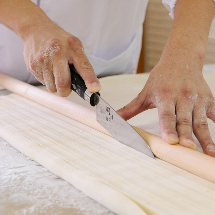 Man cutting udon dough into thin noodles