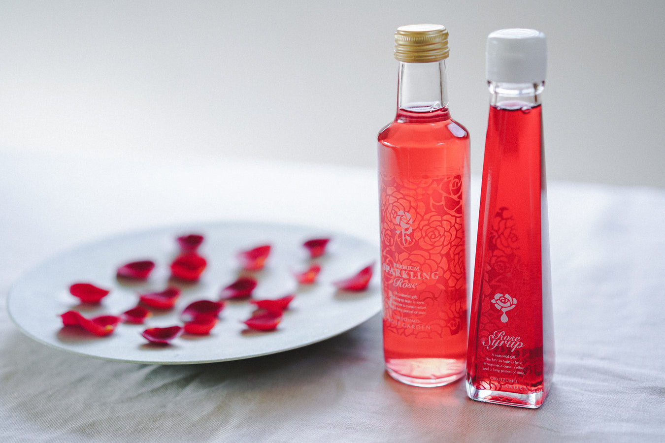 Two bottles of rose water standing next to a plate of rose petals