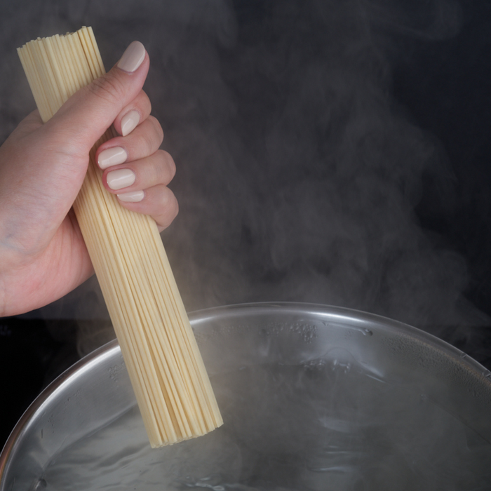 A hand placing dry ramen noodles into a pot filled with boiling water