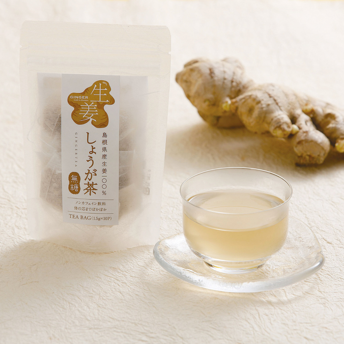 A cup of ginger tea next to package of a product and a ginger root