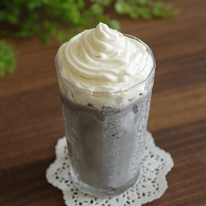 A glass of cold black sesame latte topped with whipped cream