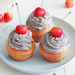 Three cupcakes topped with black sesame cream and cherries