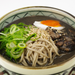 A bowl of soba noodles, scallions, braised meat and boiled egg in black sesame soup