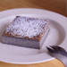 A plate of a slice of black sesame cake topped with powdered sugar