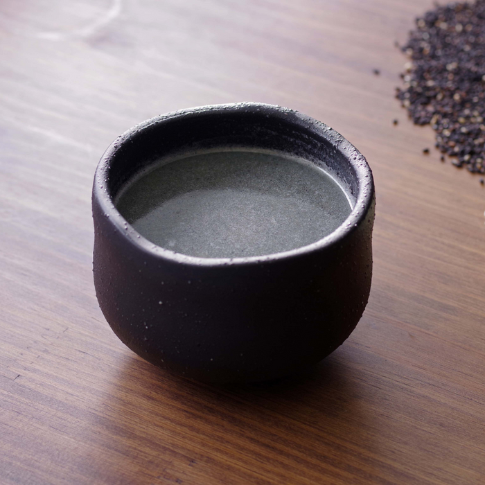 A cup of black sesame tea next to scattered black sesame seeds