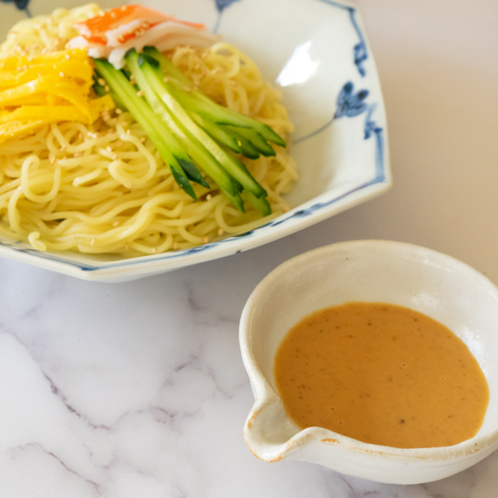 A bowl of sesame dressing next to a bowl of cold ramen noodles