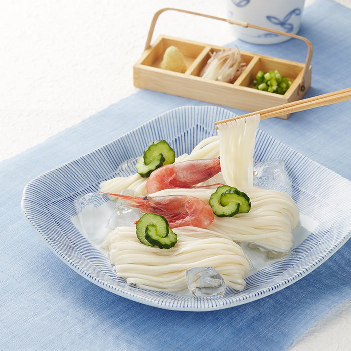Man taking cold udon noodles with chopsticks next to three kinds of garnish