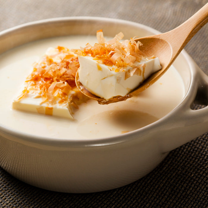 Man taking a piece of tofu topped with dried bonito flakes with spoon