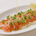 A plate of salmon carpaccio being drizzled with sesame oil