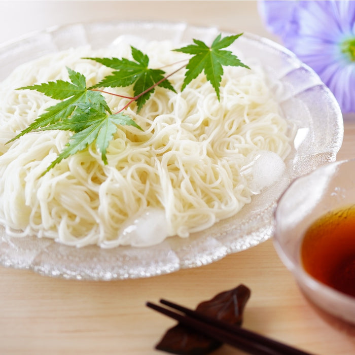 A plate of cold somen noodles next to a bowl of dipping sauce
