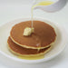 Two pancakes being poured with yuzu syrup from sauce server